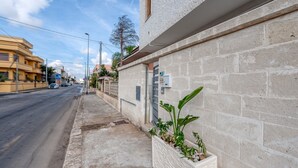 Vista de una calle con un edificio de fachada de piedra, una maceta con plantas y cielo despejado.