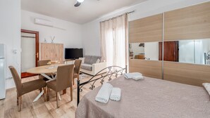 Una habitación de hotel moderna con una cama, un escritorio con silla, televisión, armario y ventilador de techo.