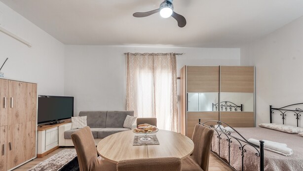 Una sala moderna con una mesa redonda de madera, un sofá, un televisor y una cama con estructura metálica.