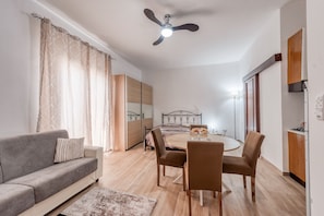 A modern living room with a sofa, dining table, chairs, a ceiling fan, and a large mirror.