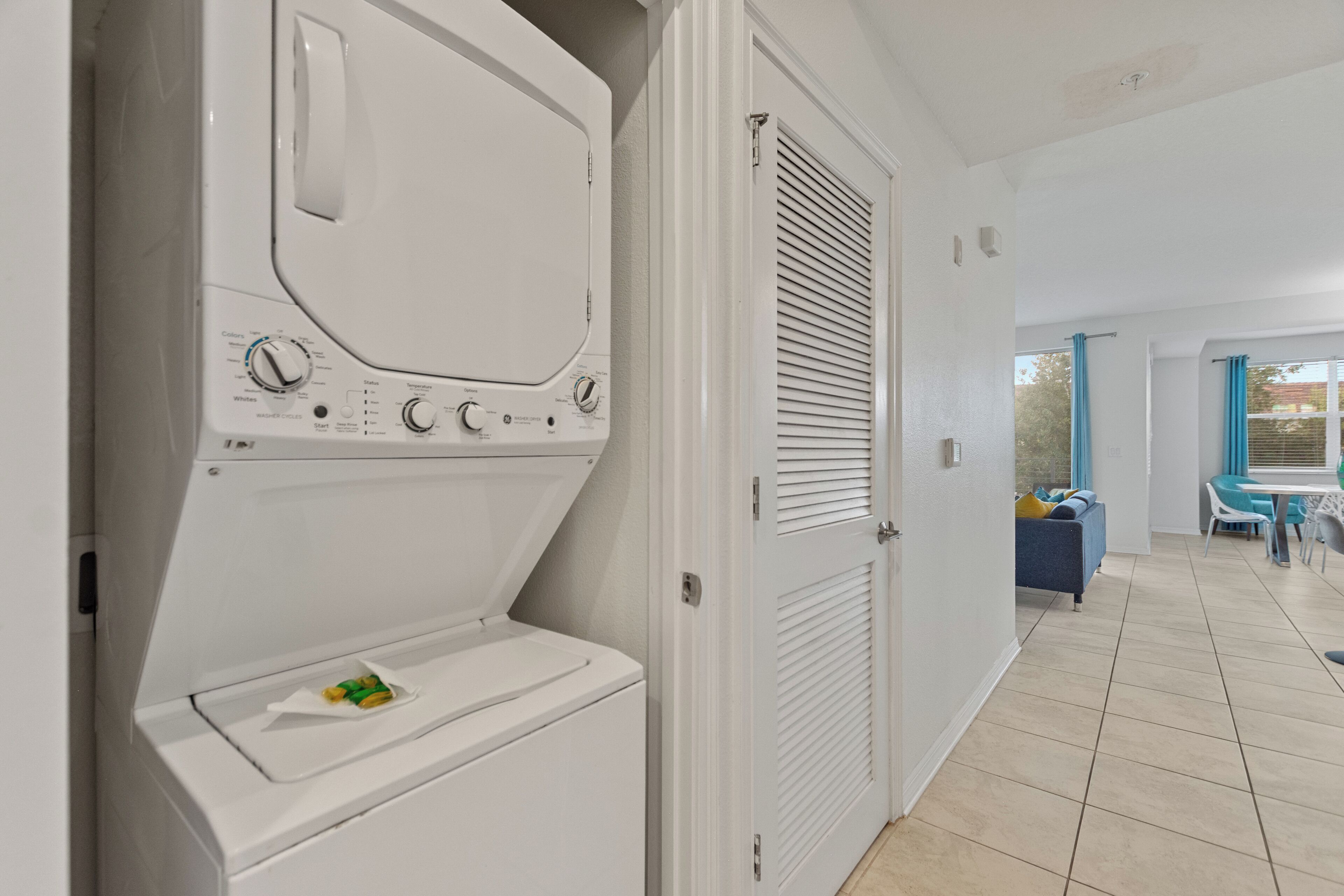 A laundry room with a front-loading washer and dryer, a door with a window, and a view of a dining area with a table and chairs.