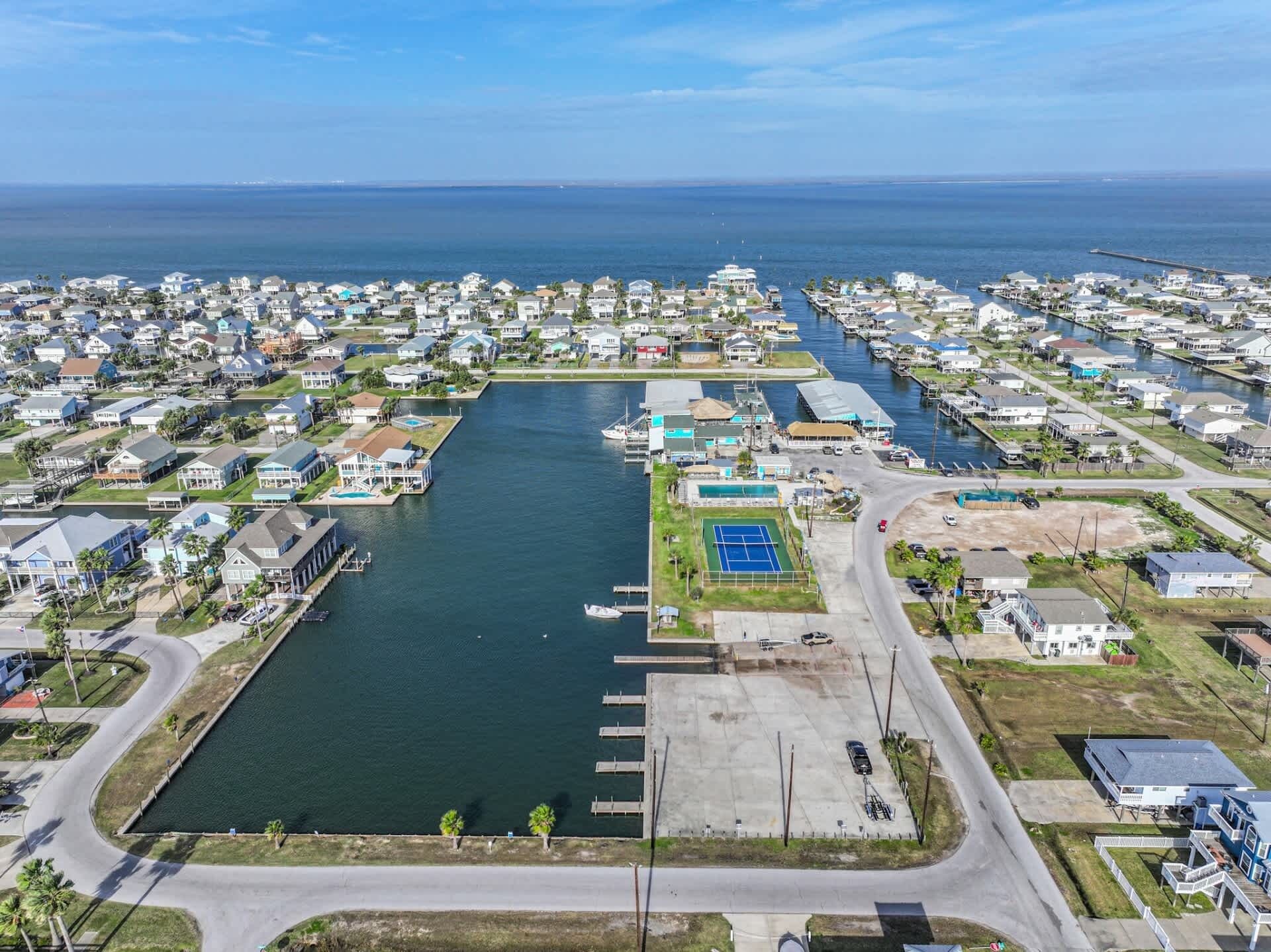 Vue aérienne d’une zone résidentielle côtière, avec un port de plaisance, des maisons et une vaste étendue d’eau.