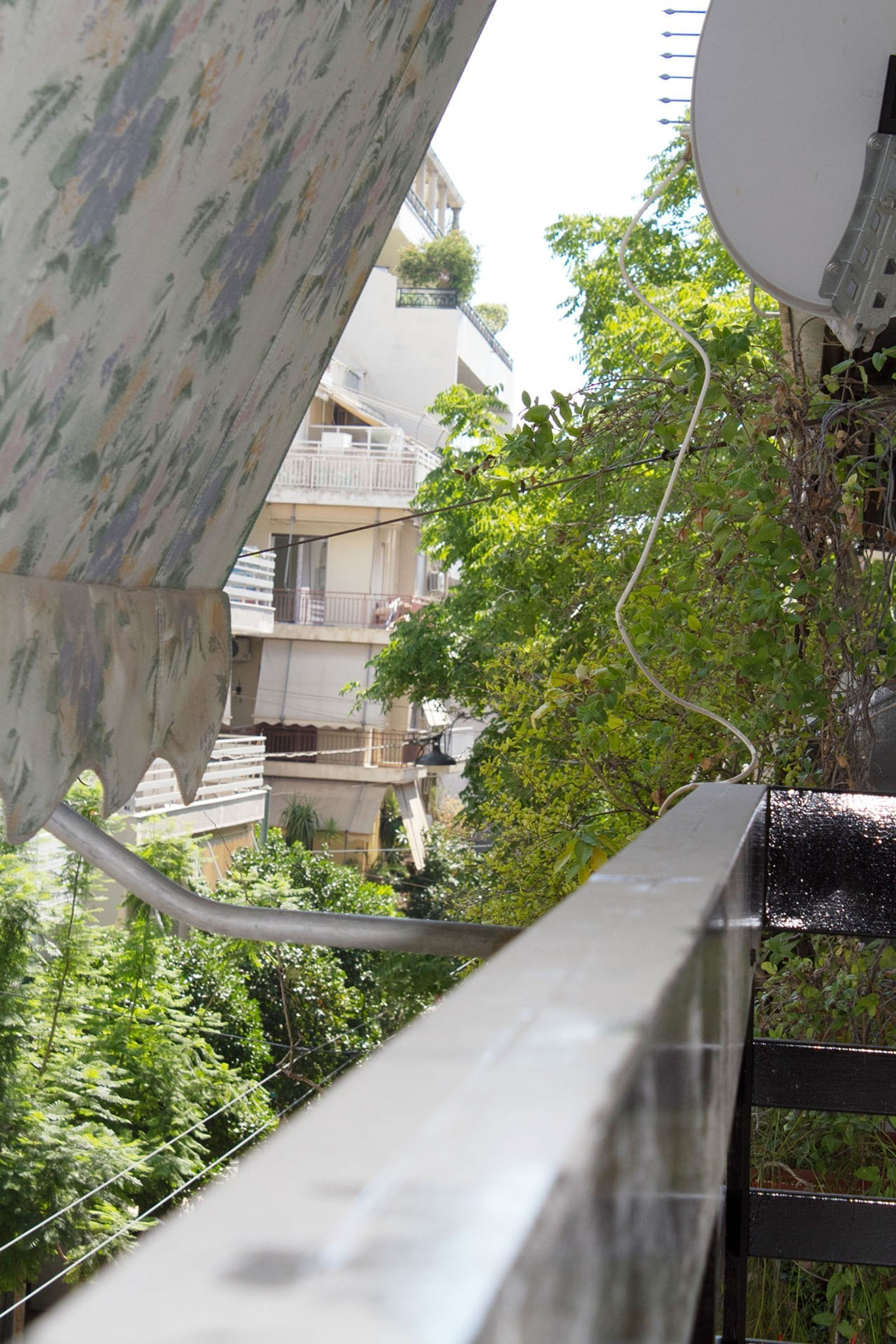A view of a balcony with a metal railing, a satellite dish, and a building with balconies in the background.