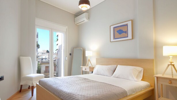 Ein modernes Hotelzimmer mit einem großen Bett, einem Sessel, einem Nachttisch mit Lampe und einem gerahmten Bild an der Wand.