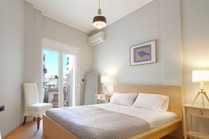 Habitación de hotel moderna con una cama grande, una silla, una mesita de noche con lámpara y un cuadro enmarcado en la pared.