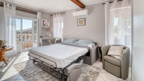 Un dormitorio con cama, una silla, un escritorio y vistas al exterior.
