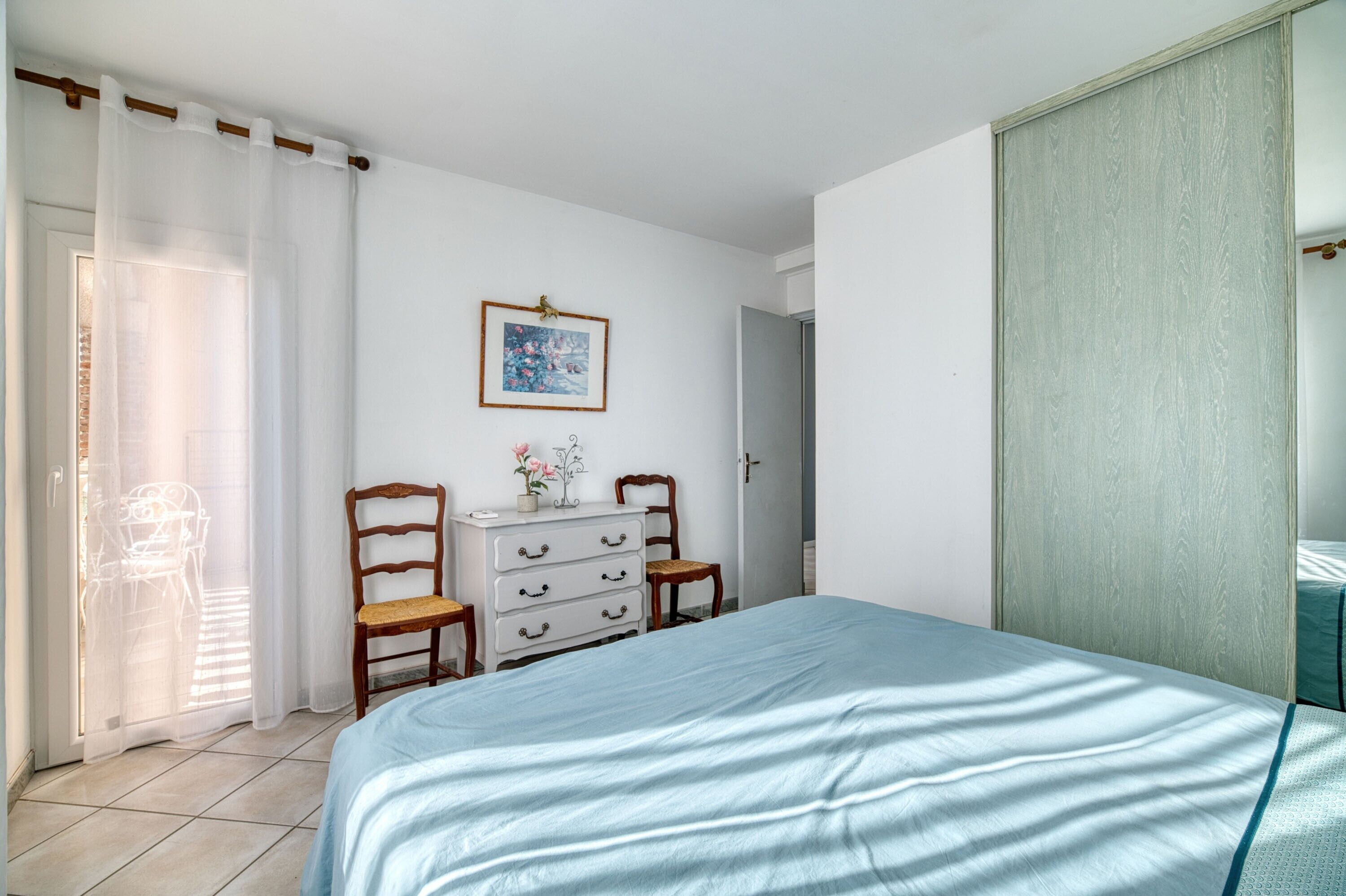 A bedroom with a bed, a dresser, a chair, a door, and a window with curtains.