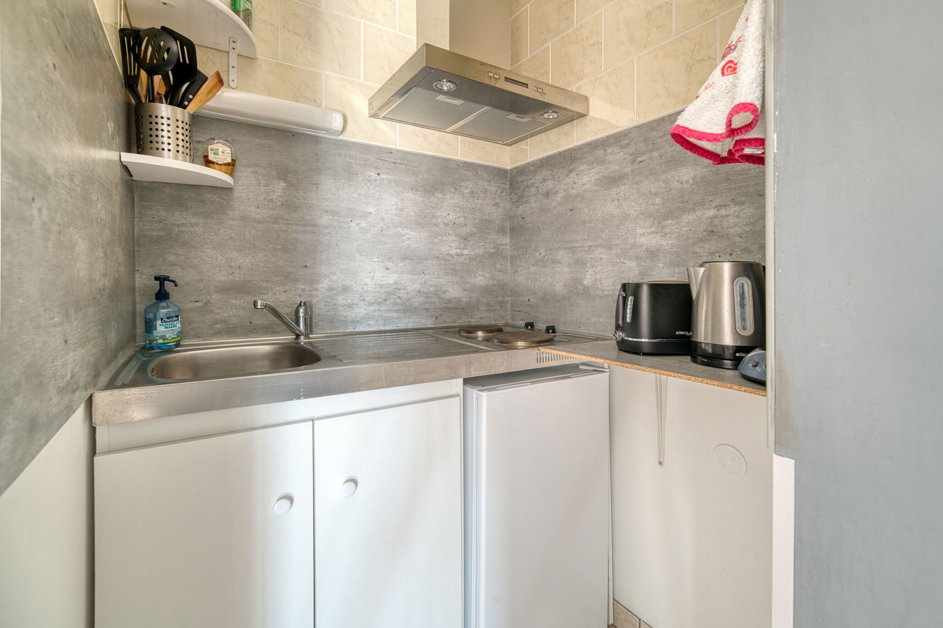 Een kleine keuken met een roestvrijstalen spoelbak, een waterkoker en een koffiezetapparaat.
