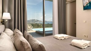 A hotel room with a bed, a chair, a view of a pool and mountains, and an exit sign. - Pietra Cave Suite with private pool (Zakynthos)