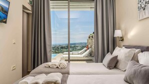 A hotel room with a bed, a sofa, a view of a cityscape, and a pool area. - Pietra Cave Suite with private pool (Zakynthos)