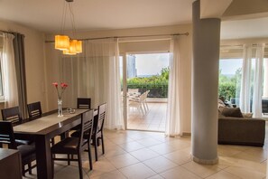 A modern dining area with a table and chairs, a vase with flowers, and a view of a balcony with outdoor furniture. - Villa Rafaella - Four Bedroom Villa, Sleeps 8 (Rethymno)