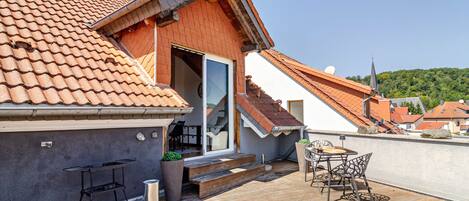 A rooftop terrace with a wooden deck, a table with chairs, and a small outdoor kitchen area.