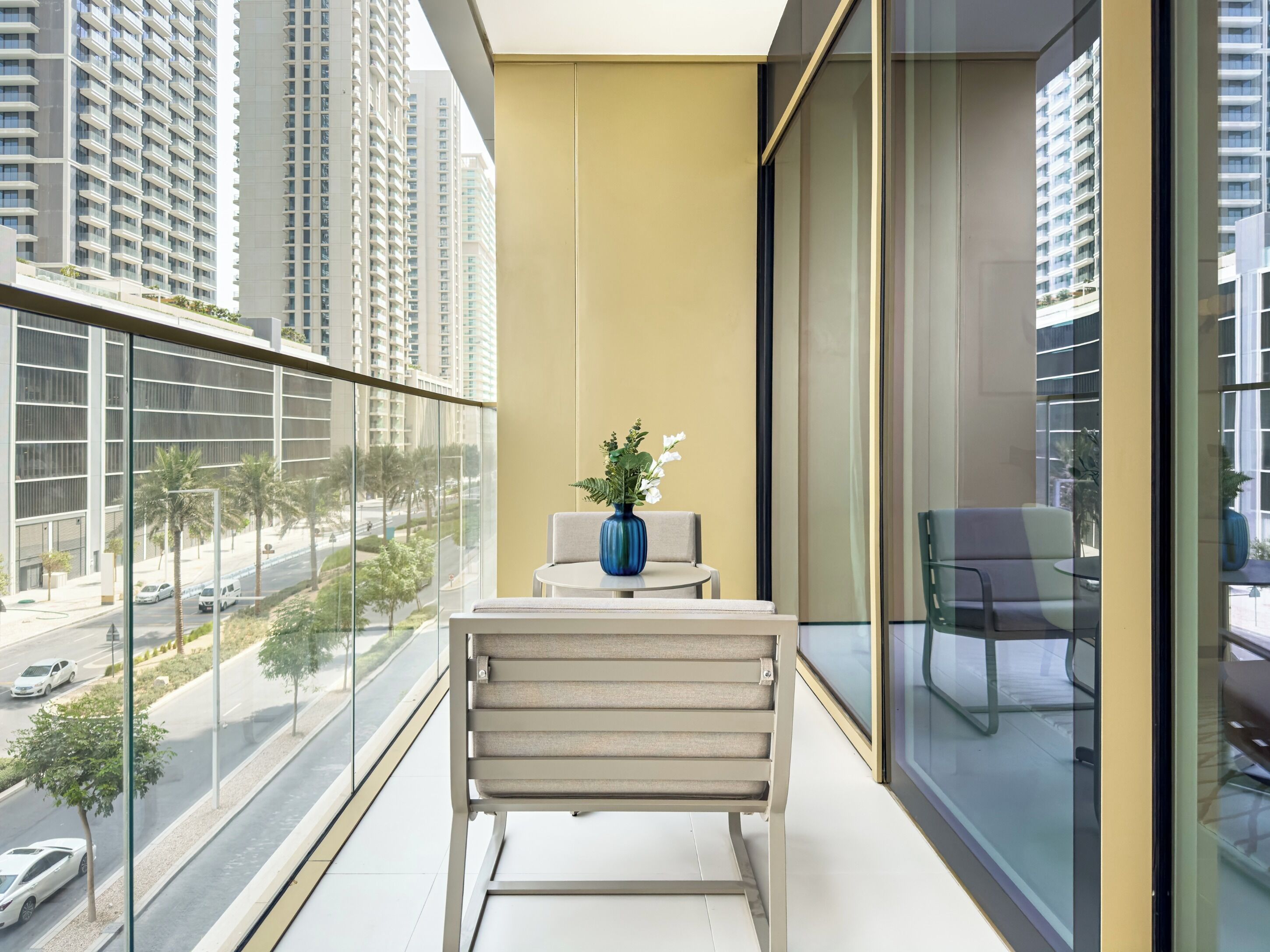 Un balcone con vista su edifici alti, una sedia, un tavolino e un vaso con fiori.