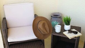 A wicker chair with a white cushion, a woven hat, a small table with a potted plant, a white pitcher, and a book with sunglasses on it. - Sand Dollar Point - Pool, Bay, Hot Tub, 10 min to beach (St. Petersburg)