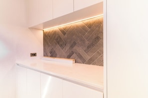 Een moderne keuken met witte kasten, een backsplash van mozaïektegels en verlichting onder de kast.