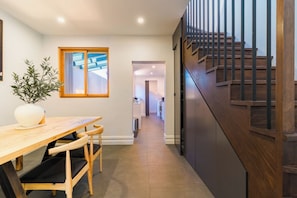 Een modern interieur met een houten eettafel, stoelen, een potplant, een trap met houten leuningen en uitzicht op een aangrenzend keuken.