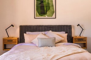 A neatly made bed with multiple pillows, a dark headboard, and two bedside tables with lamps.
