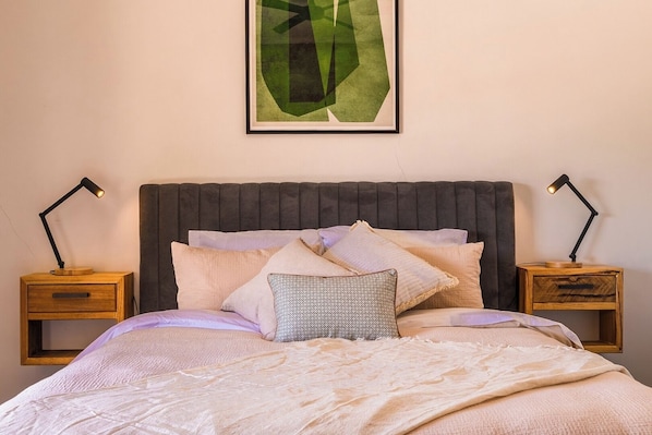 A neatly made bed with multiple pillows, a dark headboard, and two bedside tables with lamps.
