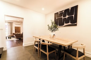 A dining area with a wooden table and chairs, a potted plant, and a large abstract artwork on the wall.