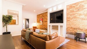 Ein modernes Wohnzimmer mit einem braunen Ledersofa, einem flachbildfernseher an einer Ziegelwand und einer Treppe, die in eine weitere Ebene führt.