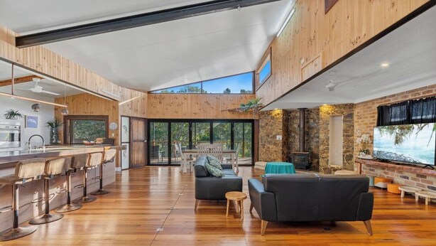 A spacious open-plan living area with a kitchen, bar seating, and a fireplace. - Large Beach Retreat with Ocean Breeze and Style (Hastings Point)