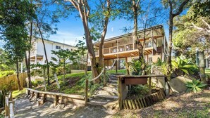 A modern building with a covered outdoor area, a wooden deck, and a stone pathway. - Large Beach Retreat with Ocean Breeze and Style (Hastings Point)