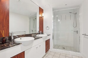 A modern bathroom with two sinks, a shower, and a large mirror.