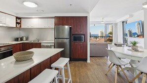 A modern kitchen with a central island, wooden cabinets, stainless steel appliances, and a dining area with a view of the city. - Oceanview 2BR apartment in the heart of Surfers Paradise (Surfers Paradise)