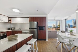 Een moderne keuken met een centraal eiland, houten kasten, roestvrijstalen apparatuur en een eetgedeelte met uitzicht op de stad.