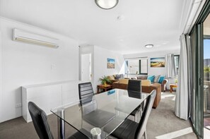 A modern room with a glass dining table, chairs, a sofa, and a large window.