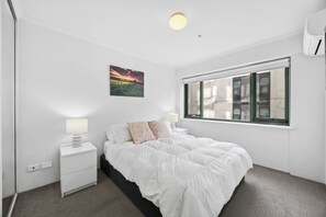A bedroom with a bed, nightstand, lamp, window, and a painting on the wall.