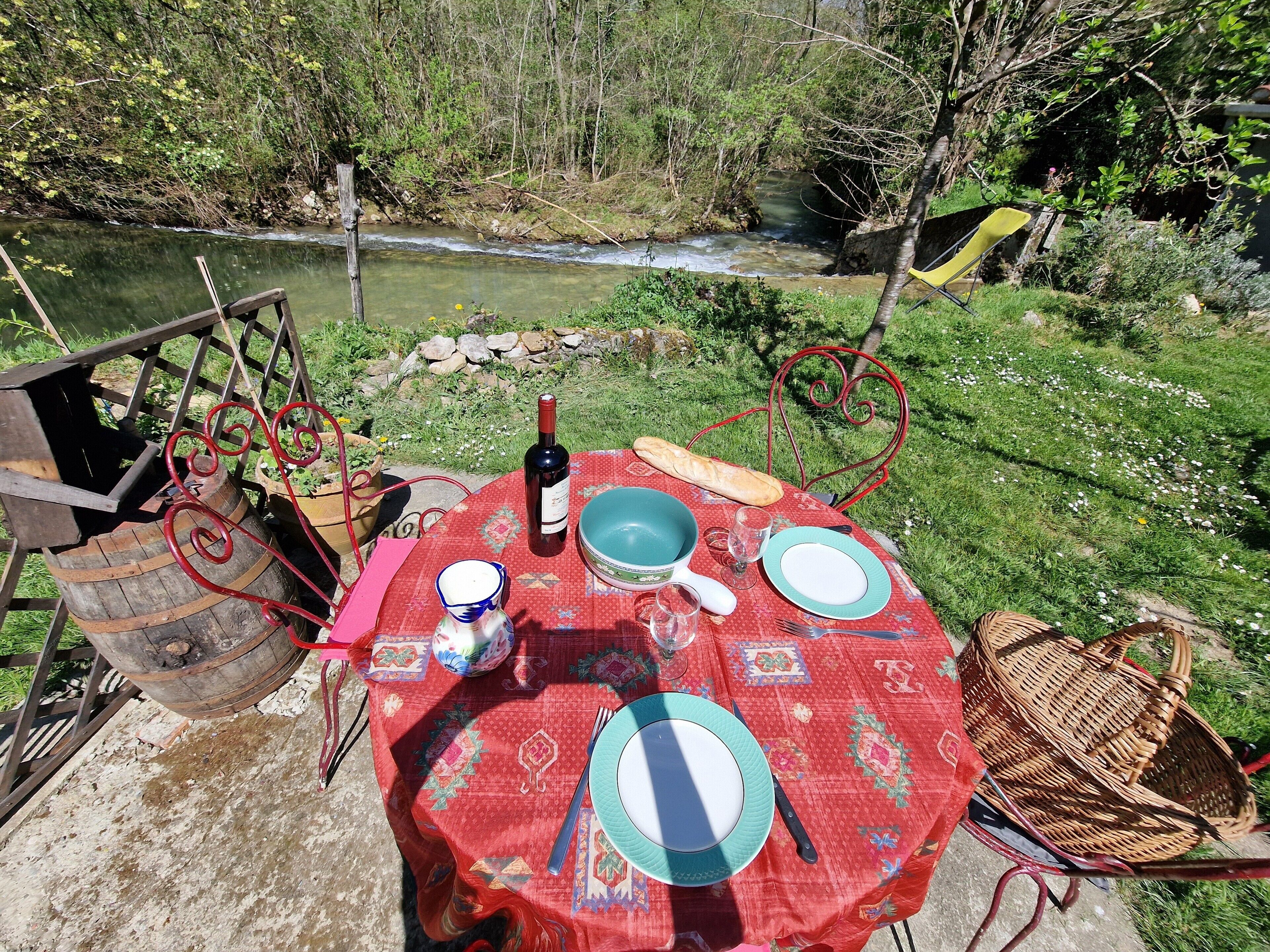 A table set outdoors with a bottle of wine, plates, and cutlery.