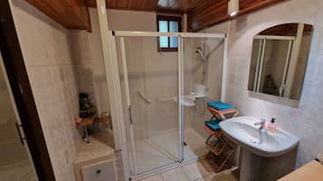 Un baño con ducha de mampara de vidrio, lavabo, espejo y suelo de madera.