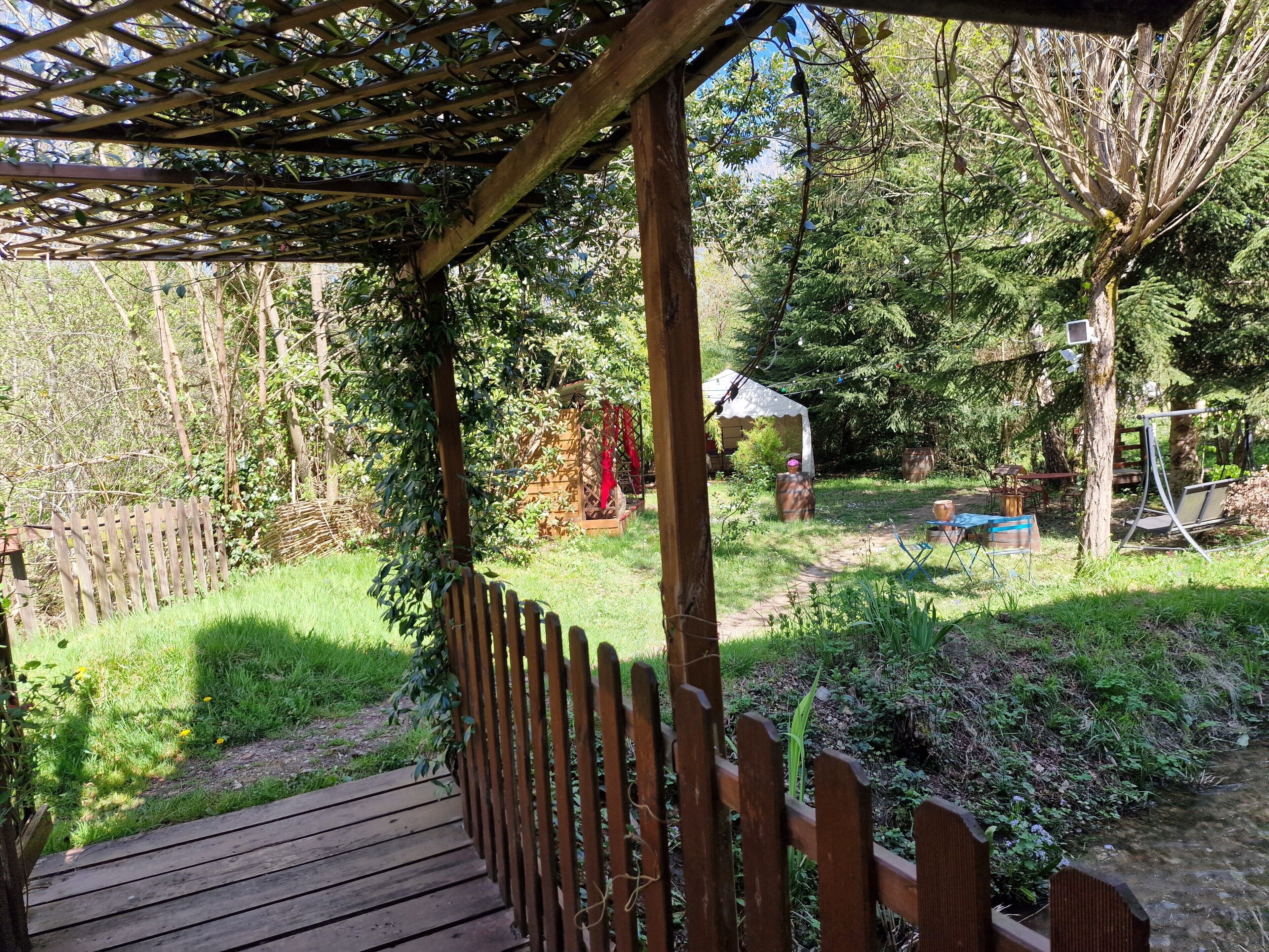 A wooden pergola with a wooden deck, surrounded by greenery and trees.