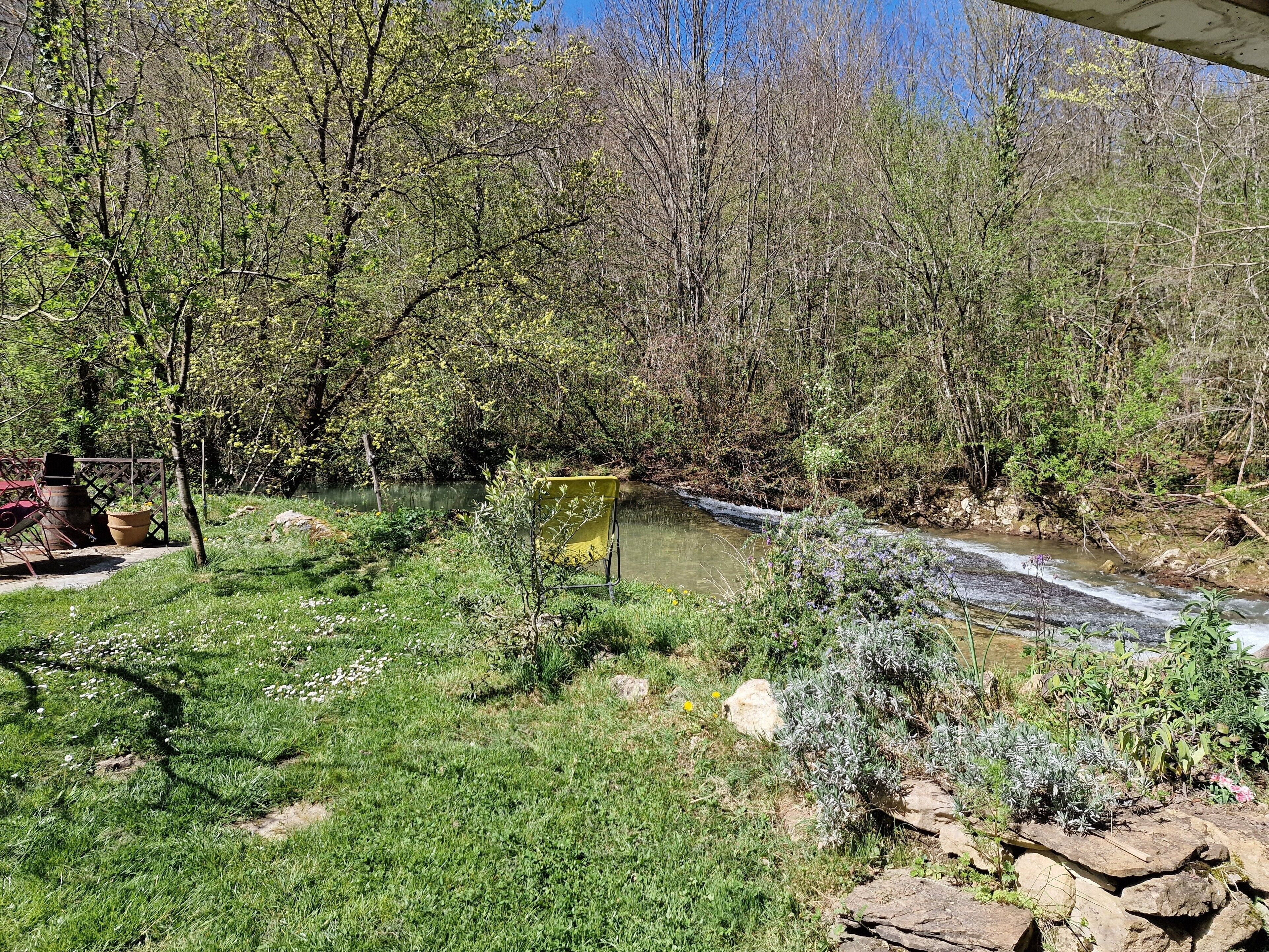 A river flowing through a wooded area with a small bridge and a yellow chair.
