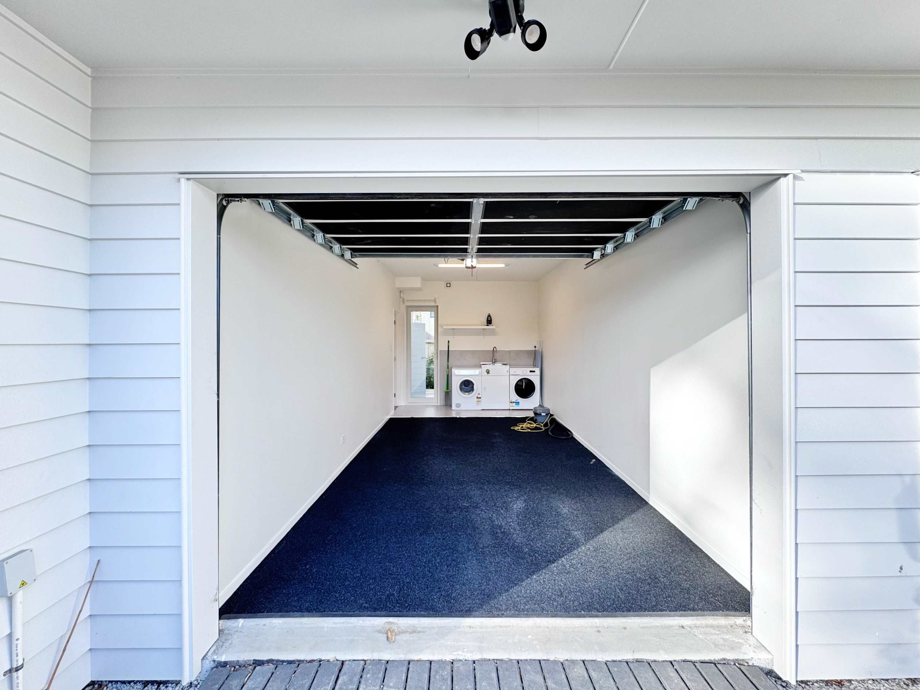 A garage with a washing machine and dryer, a door leading to a house, and a blue carpet.