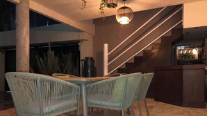 An outdoor dining area with wicker chairs and a stone floor, a staircase, and a kitchen area with a bar. - Mini depa loft (Zapopan)