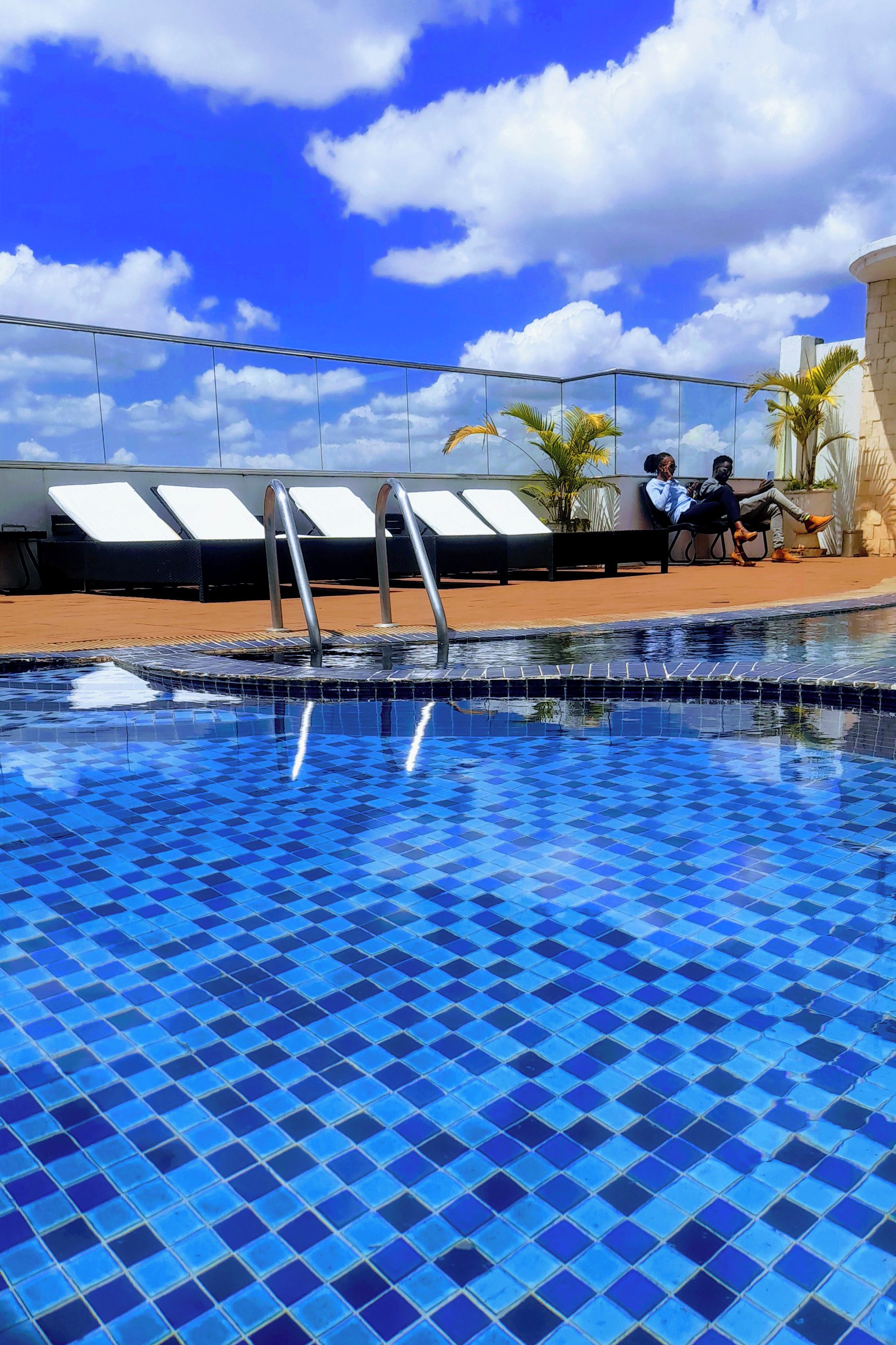 A swimming pool with blue tiles, lounge chairs, and a clear sky.