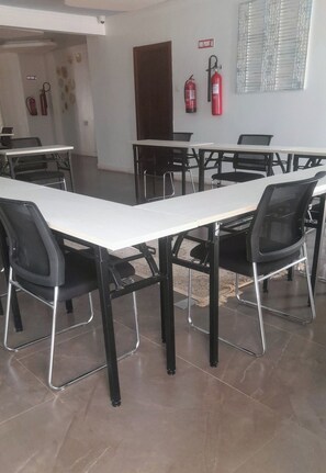 A conference room with tables and chairs, a fire extinguisher, and a fire hose on the wall.