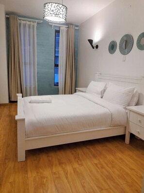 A neatly made bed in a room with a wooden floor, a window with curtains, and wall-mounted decorative plates.
