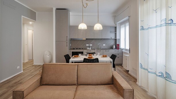 A modern kitchen with a dining area, featuring a sofa, pendant lights, and a view of the outside. - Quinto Modern Flat by Wonderful Italy (Genoa)