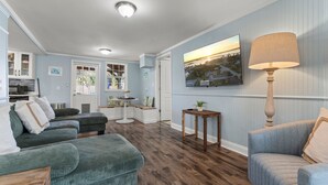 A living room with a wooden floor, a green sofa, a blue armchair, and a lamp. - St. Augustine 3-bed, Walk to Beach, Pool, Hot Tub, Tiki & Golf Green (St. Augustine)