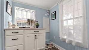 A kitchen with white cabinets, a window with sheer curtains, and a wooden floor. - St. Augustine 3-bed, Walk to Beach, Pool, Hot Tub, Tiki & Golf Green (St. Augustine)