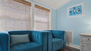 A room with a blue upholstered sectional sofa, a white dresser, and a painting on the wall. - St. Augustine 3-bed, Walk to Beach, Pool, Hot Tub, Tiki & Golf Green (St. Augustine)