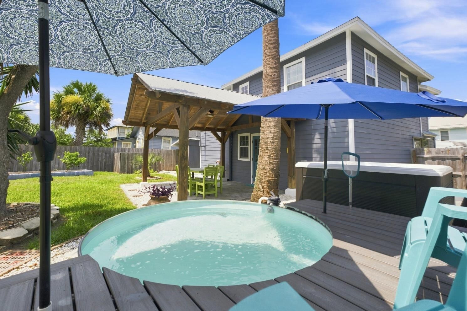 A backyard with a hot tub, wooden deck, patio furniture, and a covered seating area.