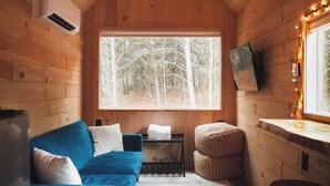 Ein gemütliches Cabin-Interieur mit einem blauen Sofa, einem kleinen Tisch, einem Fenster mit Blick auf Bäume und einer Holzboden.