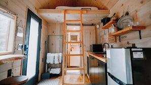 Una cocina compacta con paredes de madera, una escalera que lleva a un altillo, un refrigerador y un lavamanos.