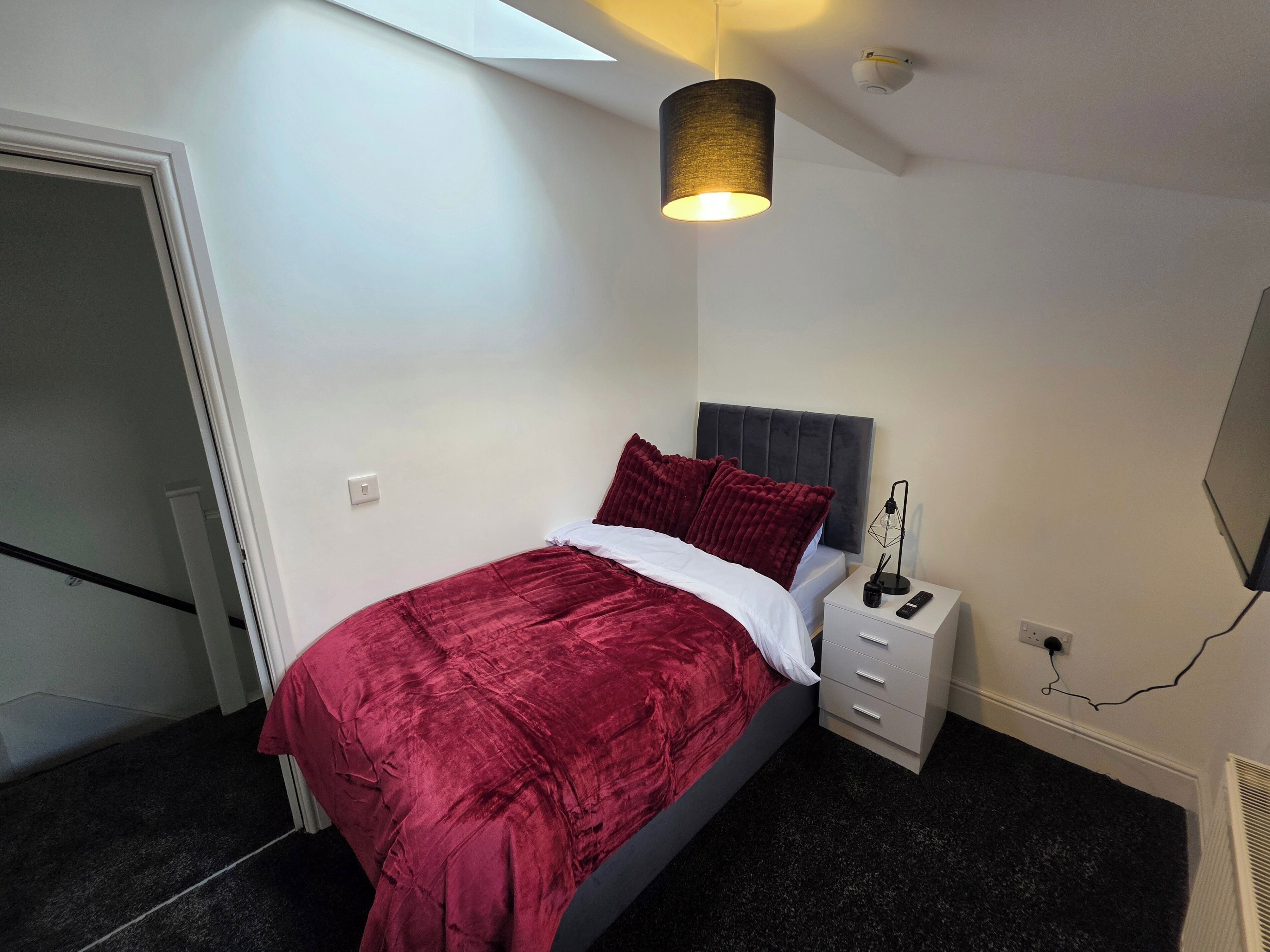 Un dormitorio con cama, mesita de noche, lámpara y luz de techo.