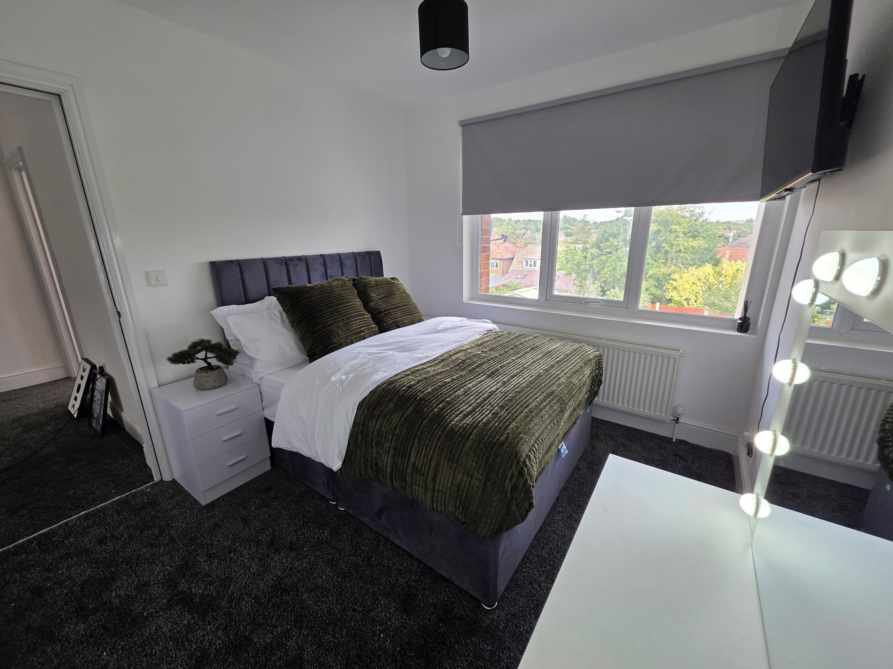 Un dormitorio con cama, mesita de noche, cómoda, ventana con vistas y tocador con iluminación.