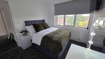 Un dormitorio con cama, mesita de noche, cómoda, ventana con vistas y tocador con iluminación.